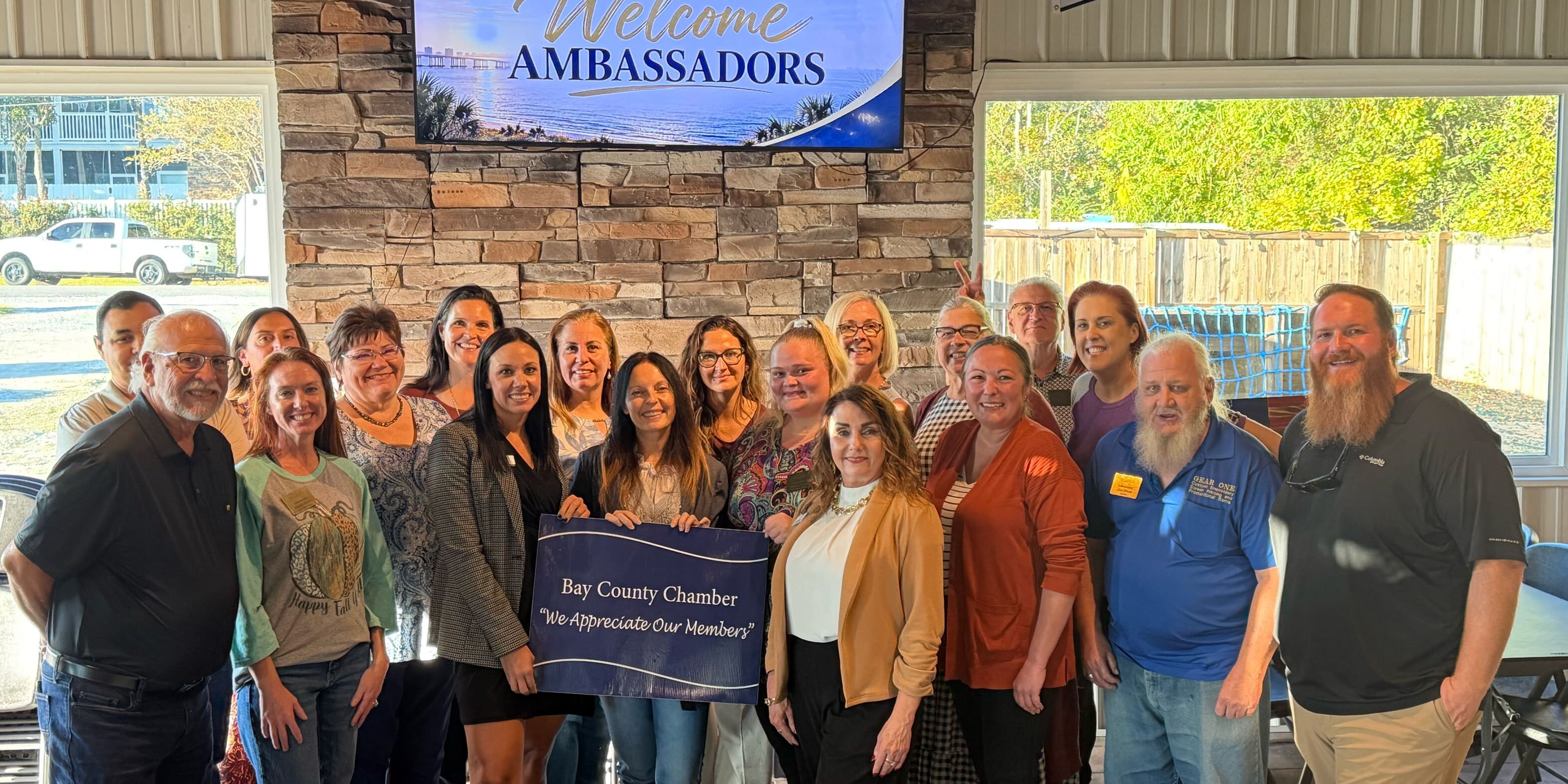 Bay County Chamber of Commerce Ambassadors gather for a group photograph beneath a Welcome Ambassadors display, holding a We Appreciate Our Members sign.