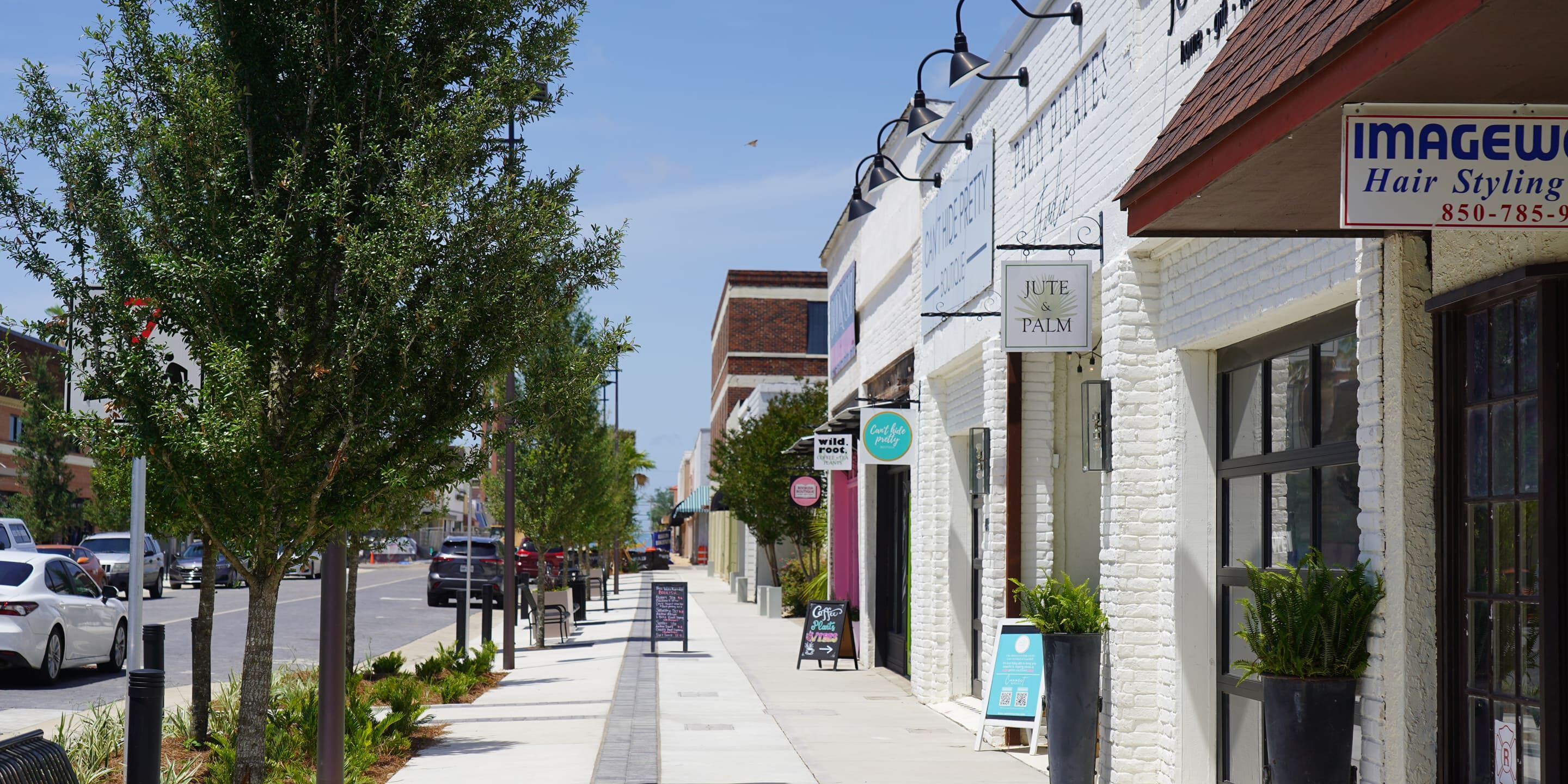 Local shops and small business storefronts along a tree-lined sidewalk in downtown Panama City, Florida.